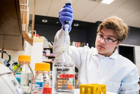 A student researcher measuring liquid into a bottle at a lab bench